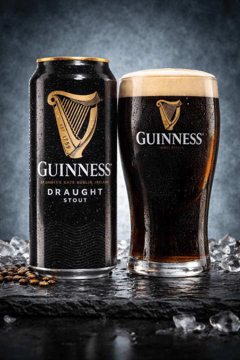 Guinness Draught Stout Dose 440ml neben Glas mit cremiger Schaumkrone auf Eis
